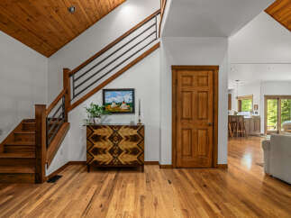Step into this inviting entryway featuring a stunning wooden staircase with modern metal railings, leading up to a vaulted wood-paneled ceiling.