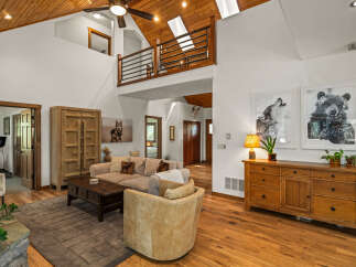 Experience rustic charm in this spacious living room featuring a vaulted wood-paneled ceiling with skylights and a loft overlooking the area.