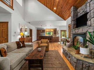 Experience rustic charm in this inviting living space, featuring a grand stone fireplace and a vaulted wood-paneled ceiling.