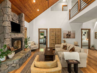 Experience rustic charm in this spacious living room, featuring a grand stone fireplace and a soaring wood-paneled vaulted ceiling.