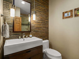 This modern bathroom features a sleek white vessel sink atop a dark wood vanity, complemented by a striking stacked stone accent wall.