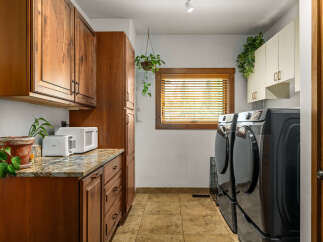This laundry room boasts ample storage with custom wooden cabinetry and overhead cabinets, perfect for organizing supplies.