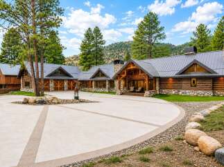 Experience luxury mountain living in this stunning log home, featuring a grand entrance with a stone-clad fireplace and exposed wooden beams.