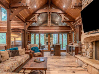 Experience rustic luxury in this stunning log cabin living room, featuring a grand stone fireplace and soaring vaulted ceilings with exposed wooden beams.