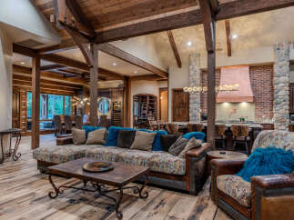 Experience rustic luxury in this expansive living space, featuring a grand sectional sofa adorned with plush blue pillows and a rustic coffee table.