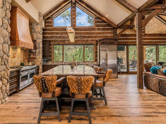 Experience rustic luxury in this stunning mountain lodge kitchen, featuring a massive stone fireplace, a copper range hood, and a large granite island perfect for entertaining.