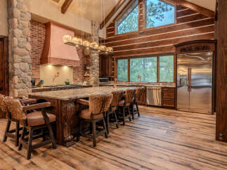 Experience rustic luxury in this stunning log cabin kitchen, featuring a grand granite island with unique animal-hide bar stools.