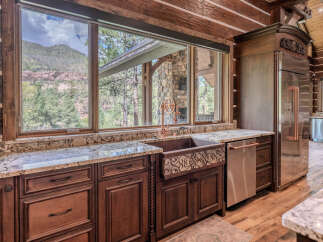 Experience rustic luxury in this stunning log cabin kitchen, featuring a large copper farmhouse sink with intricate detailing and a unique vintage-style faucet.