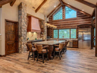Experience rustic luxury in this stunning mountain kitchen, featuring a grand stone island with comfortable seating and a striking copper range hood.