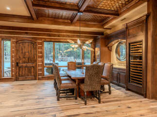 Experience rustic luxury in this stunning dining room, featuring a grand wooden door and expansive windows that frame a picturesque forest view.