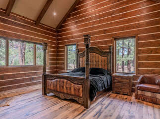 Experience rustic luxury in this stunning log cabin bedroom, featuring a grand four-poster bed with ornate carvings and a textured headboard.