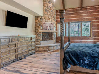 Experience rustic luxury in this stunning bedroom featuring a grand stone fireplace and a cozy log-paneled wall.