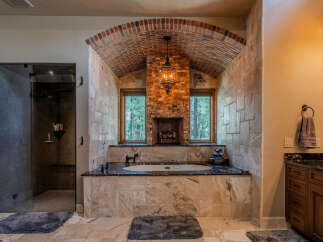 Indulge in luxury in this stunning master bathroom, featuring a deep soaking tub set against a backdrop of a charming brick fireplace and arched ceiling.