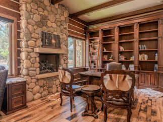 Experience rustic elegance in this stunning home office, featuring a grand stone fireplace and custom built-in bookshelves.