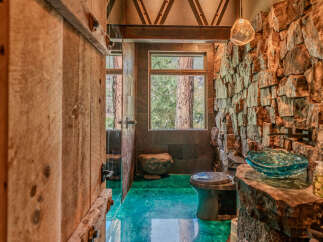 Experience rustic luxury in this unique bathroom, featuring a striking stone accent wall and a vibrant, emerald-green epoxy floor.