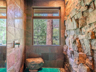 Experience the ultimate in natural luxury with this stunning bathroom featuring a unique stone accent wall and a large window overlooking a serene forest.