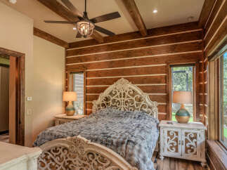 Experience rustic luxury in this charming bedroom featuring a stunning log-style wood-paneled accent wall and exposed wooden beams.