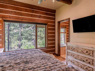 Experience rustic luxury in this stunning bedroom featuring a cozy log-style accent wall and a large window framing breathtaking forest views.