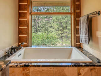 Experience ultimate relaxation in this luxurious bathroom featuring a deep soaking tub with a scenic view of the surrounding pine forest.