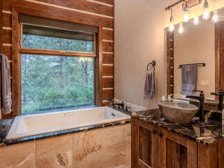 Experience rustic luxury in this stunning bathroom featuring a deep soaking tub with a picturesque forest view.