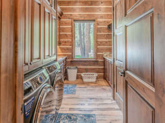 Experience rustic charm in this spacious laundry room, featuring a stacked washer and dryer set against a backdrop of warm log walls.