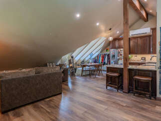 Discover this charming attic living space, featuring a cozy living area with a plush sofa and a well-appointed kitchenette with dark wood cabinetry and granite countertops.