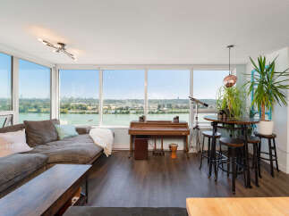 Experience breathtaking panoramic views from this stunning living space, featuring expansive windows that showcase a serene river and vibrant cityscape.
