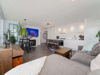 Experience modern living in this open-concept condo, featuring a sleek white kitchen with ample cabinet space and integrated appliances.