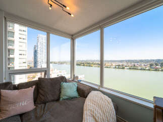 Experience breathtaking panoramic views from this stunning apartment, featuring expansive windows that showcase a serene river and a vibrant cityscape.