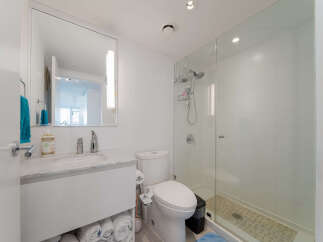 This modern bathroom features a sleek vanity with a marble countertop and ample storage, complemented by a large mirror with integrated lighting.
