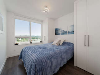 Experience comfort and style in this inviting bedroom, featuring a plush blue comforter on a cozy bed and a large window offering scenic views.