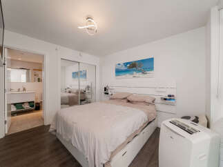 Experience modern living in this stylish bedroom featuring a comfortable bed with ample storage, mirrored closet doors, and a serene beach-themed artwork.