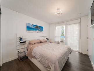 Experience comfort and style in this inviting bedroom, featuring a plush bed adorned with soft linens and a striking wall art depicting a serene beach scene.