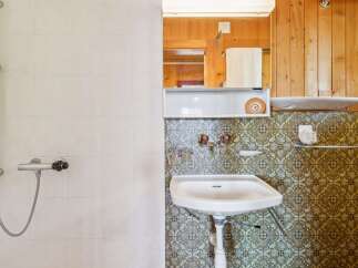 This bathroom features a tiled shower area with a chrome showerhead and controls, complemented by a patterned tiled wall surrounding the sink.