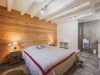 Experience cozy mountain living in this charming bedroom featuring a warm, wood-paneled accent wall and exposed white beams on the ceiling.