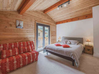 Experience cozy mountain living in this charming bedroom featuring a comfortable bed adorned with heart-shaped pillows and a red striped sofa.