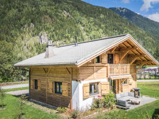 Experience the charm of this rustic wooden chalet nestled against a backdrop of lush green mountains.