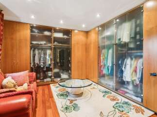 Step into this luxurious walk-in closet, featuring ample storage with elegant glass-fronted wardrobes and rich wooden cabinetry.