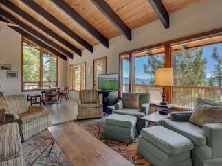 Experience breathtaking lake and mountain views from this stunning living room, featuring a vaulted wood-beamed ceiling and expansive windows.
