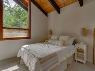 Experience serene living in this charming bedroom, featuring a large window with stunning forest views and a vaulted wood-beamed ceiling.