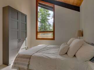Experience serene living in this charming bedroom, featuring a large window that frames a picturesque view of lush green trees.