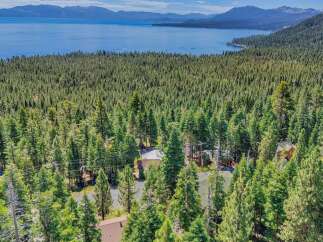 Nestled amidst a dense forest, this property offers a serene retreat with breathtaking views of a vast blue lake and distant mountains.