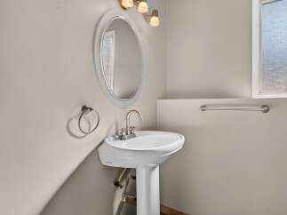 This bathroom features a sleek pedestal sink with a modern faucet, complemented by an oval mirror and a brushed nickel towel ring.