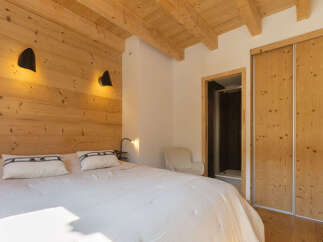 Experience rustic charm in this cozy bedroom featuring a wooden-paneled accent wall and exposed ceiling beams.