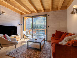 Experience mountain living in this charming chalet-style living room, featuring a cozy orange sofa and a plush armchair perfect for relaxing.