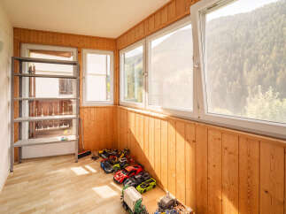 This charming room features a wall of warm, natural wood paneling, complemented by large windows that offer stunning views of a lush, green mountainside.
