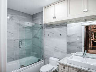 Experience modern luxury in this beautifully renovated bathroom, featuring elegant marble-look tiles and a sleek glass-enclosed shower over a pristine white bathtub.