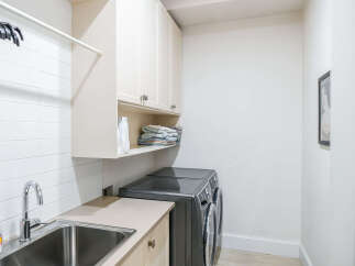 This laundry room features a sleek stainless steel sink with a modern faucet, complemented by white subway tile backsplash.
