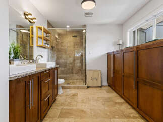 Experience luxury in this spacious bathroom featuring dual vessel sinks atop a granite countertop and rich wood cabinetry.