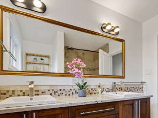 This beautifully appointed bathroom features a spacious vanity with dual sinks, complemented by a large, ornate mirror that reflects the elegant tile backsplash.